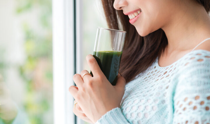 Smiling woman holding green drink.