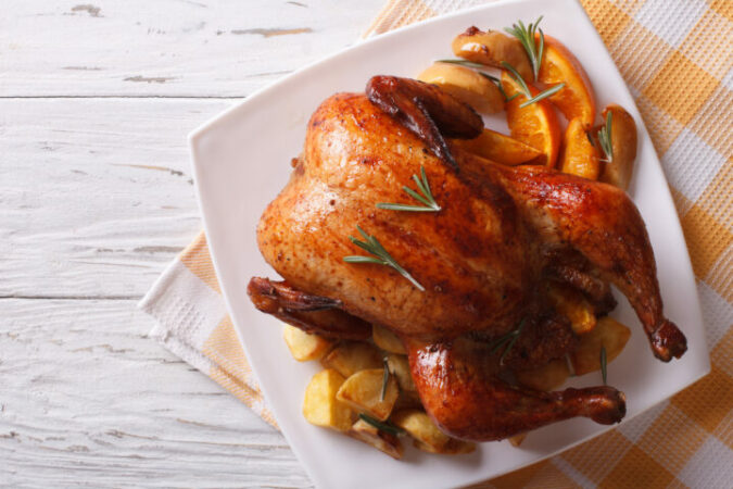 baked whole chicken with oranges and potatoes on a plate. horizontal view from above