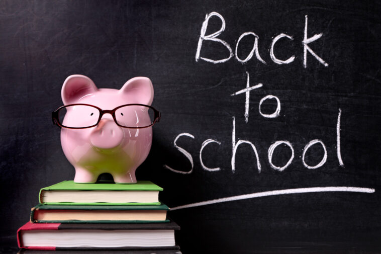 Pink piggy bank on top of a stack of three books in front of a black board with Back to School written in chalk.