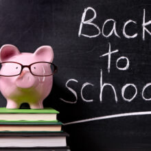 Pink piggy bank on top of a stack of three books in front of a black board with Back to School written in chalk.