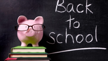 Pink piggy bank on top of a stack of three books in front of a black board with Back to School written in chalk.