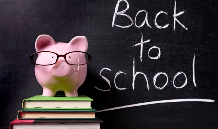 Pink piggy bank on top of a stack of three books in front of a black board with Back to School written in chalk.