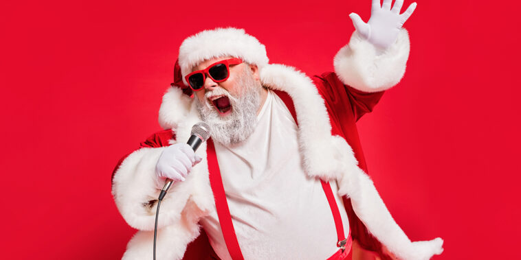 Photo of Santa Claus singing 9 classic Christmas songs on a mic.