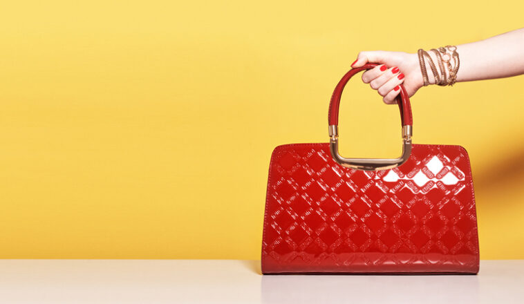 Woman's hand holding a red purse in front of a yellow background.