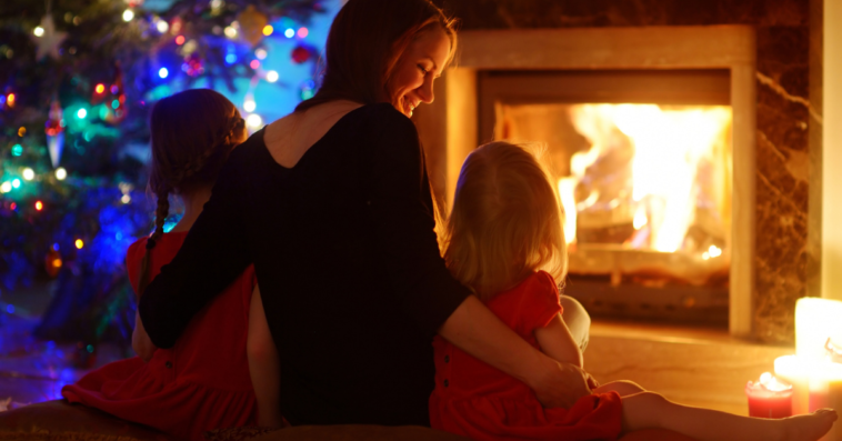 Mother sitting in front of fireplace and Christmas tree with children