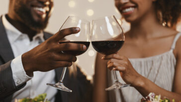 A couple clinks together two glasses of red while while smiling