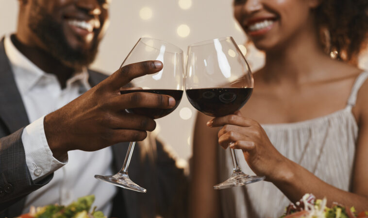 A couple clinks together two glasses of red while while smiling