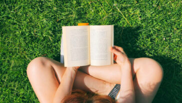 young woman sitting on the grass in park and reading the book
