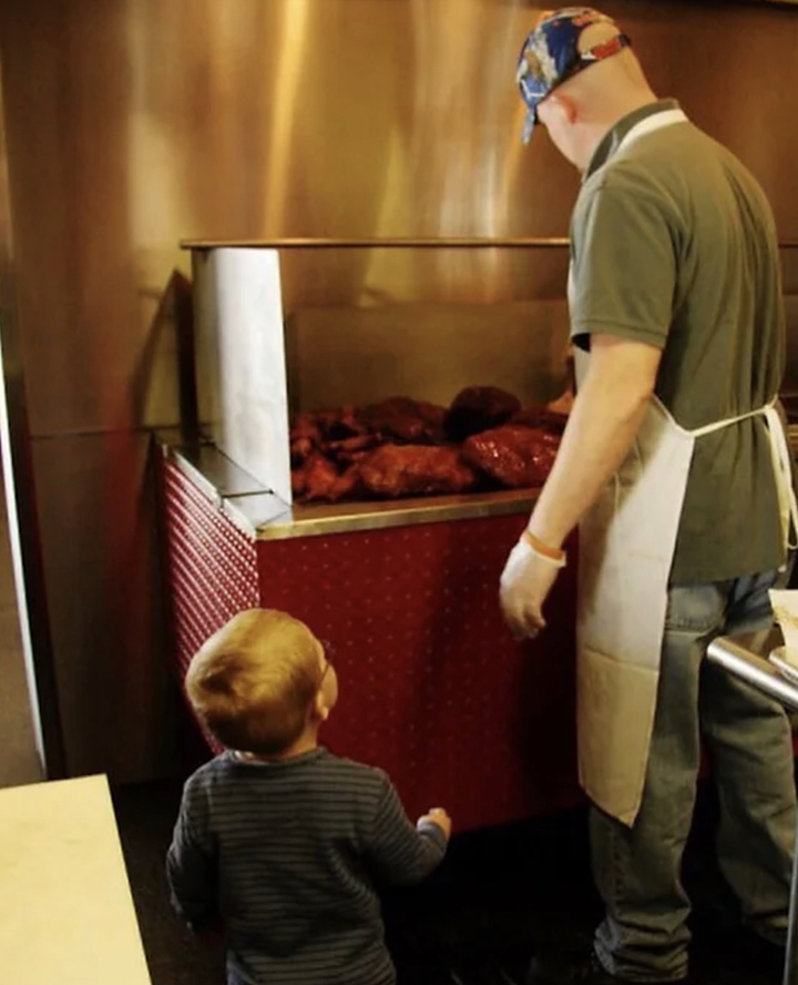 Man standing at grill, barbequing with child.