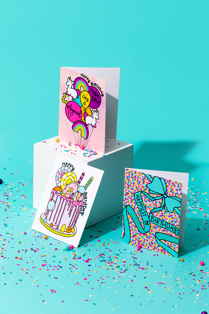 Three colorful birthday cards on top of a white box in front of a blue background.