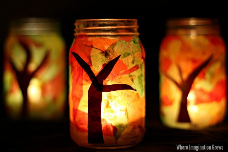 Mason jars decorated with tree branches, colorful tissue paper, and lit candles.