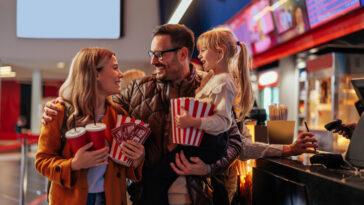 Two parents at the movie theater with their child, excited to see a movie on National Cinema Day.