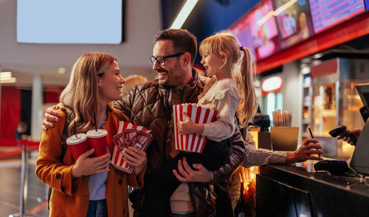 Two parents at the movie theater with their child, excited to see a movie on National Cinema Day.