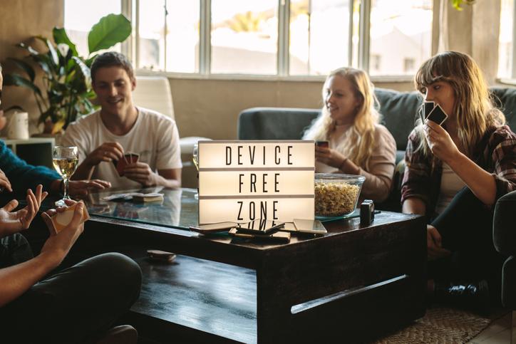 group of friends playing cards indoors at device free zone. Cell phones on table with young men and woman hanging out together. holiday detox