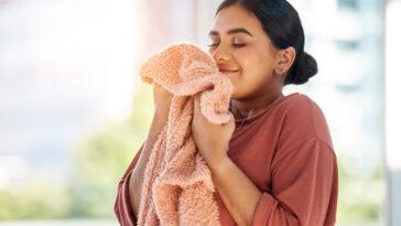 Woman smelling clean laundry, blanket or fabric for fresh and clean smell in house after doing washing, cleaning and housekeeping. Happy female cleaner with textile for aroma, fragrance and scent bath and body works