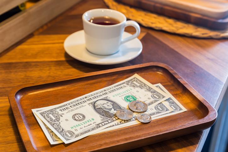 Dollar bills, coins and coffee on a table to represent the concept of tipping culture.