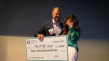 Two people holding a large check. The man is smiling and the woman is hiding her face.