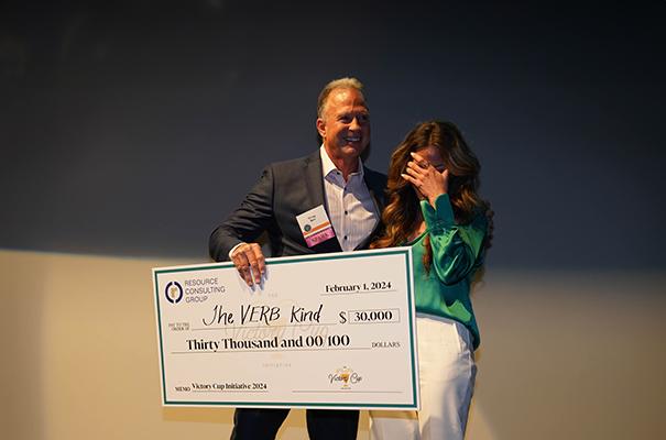 Two people holding a large check. The man is smiling and the woman is hiding her face.