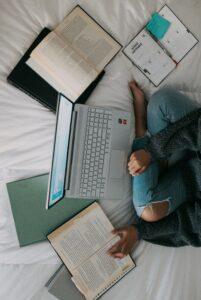 woman in blue long sleeve shirt and blue denim jeans sitting on bed using laptop
