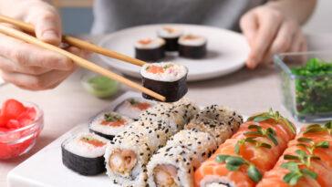 Woman taking tasty sushi roll with salmon from set at table, closeup