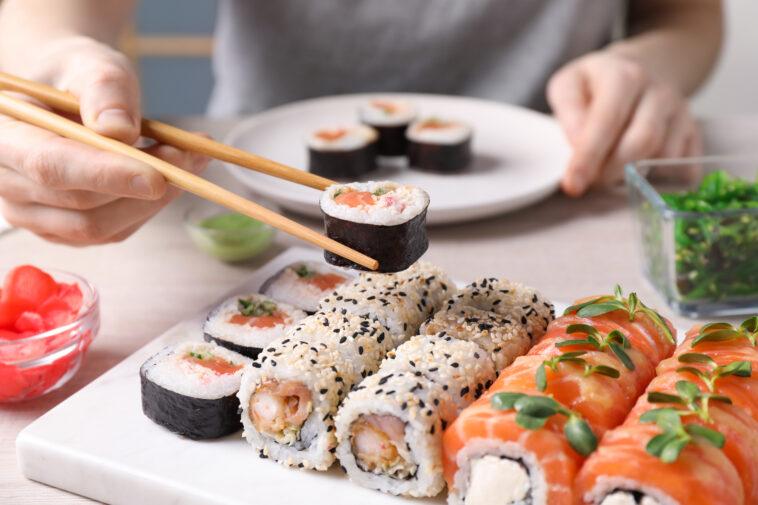 Woman taking tasty sushi roll with salmon from set at table, closeup