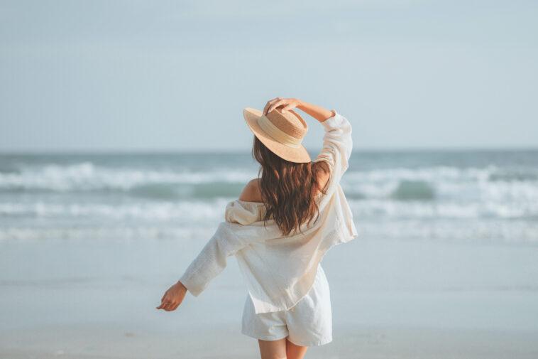 Summer beach vacation concept, Young woman with hat relaxing with her arms raised to her head enjoying looking view of beach ocean on hot summer day, copy space.