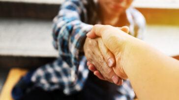 Close-up handshake for help homeless man on walking street in the capital city.