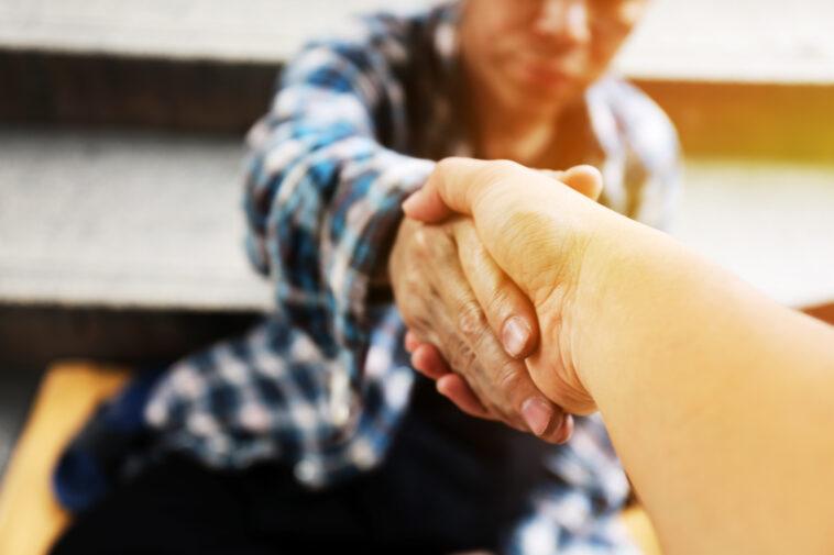 Close-up handshake for help homeless man on walking street in the capital city.