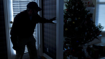 This photo illustrates a burglary or thief breaking into a home at night through a back door during the Christmas Holiday Season.