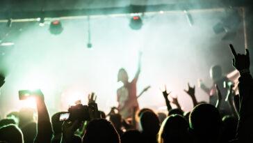 People raising hands at the rock show. Audience in front of the stage. Live rock concert. Rock musicians on the stage