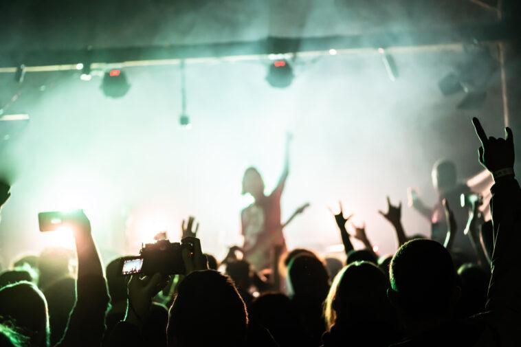 People raising hands at the rock show. Audience in front of the stage. Live rock concert. Rock musicians on the stage